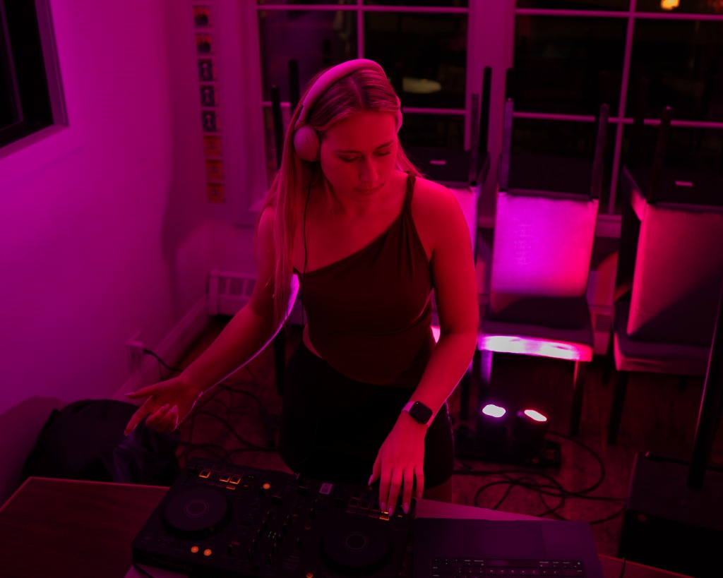 Female DJ with headphones performing under pink and magenta nightclub lighting on Prince Edward Island - Eastside Photography promo shoot