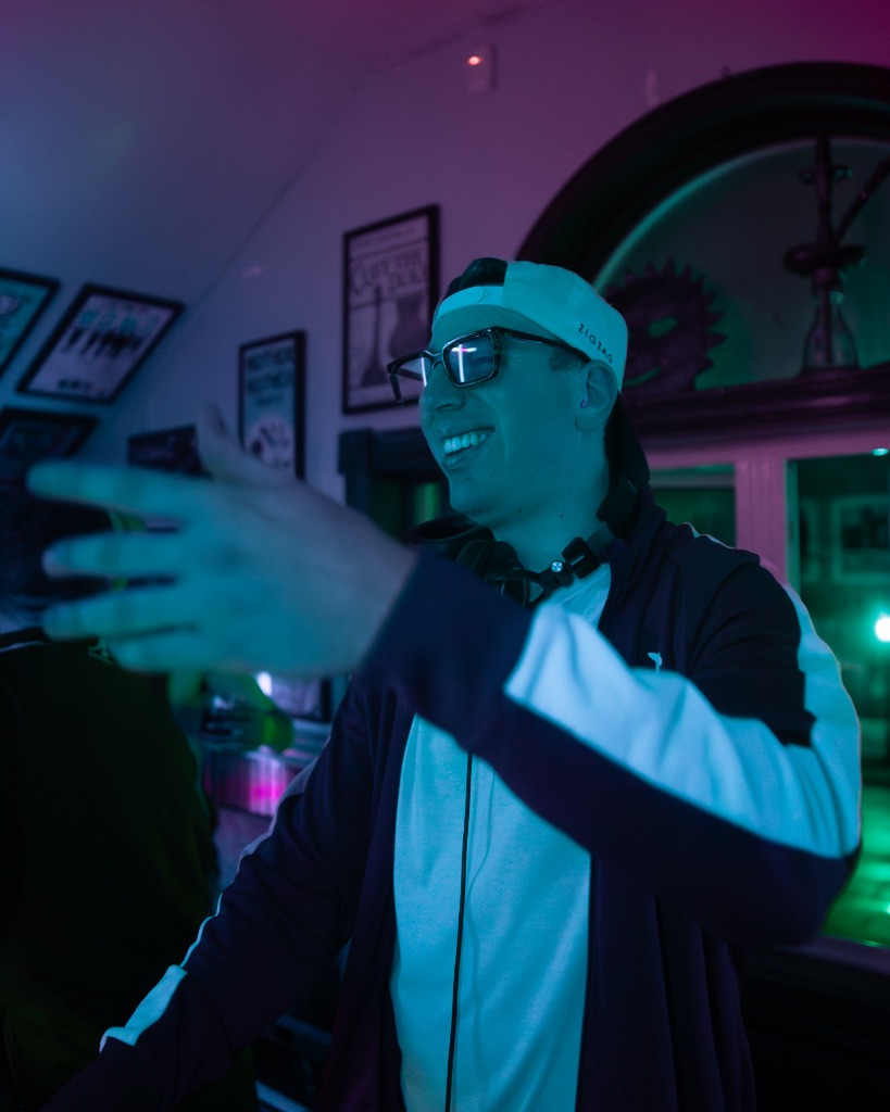 DJ smiling on stage wearing glasses under teal spotlights in PEI - Eastside Photography creative event portrait