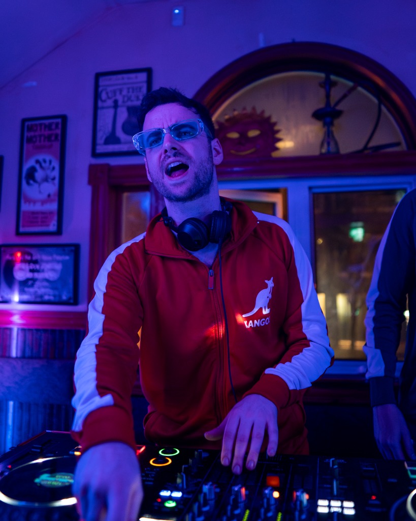 Moody promo portrait of DJ on decks under pink and blue nightclub wash lighting - Eastside Photography PEI artist promotion