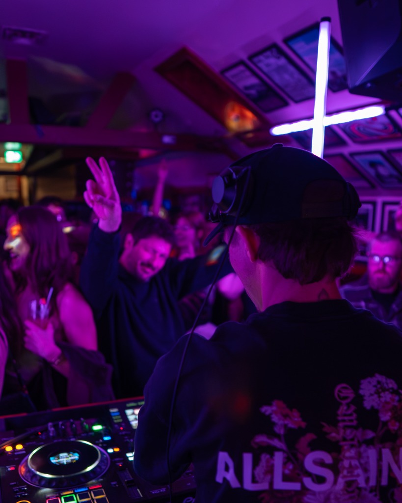 DJ performing at a PEI club with hand raised high surrounded by glowing neon tube frames - Eastside Photography live event