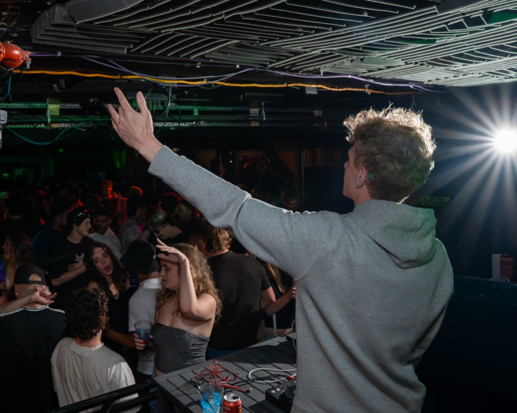 DJ raising hand to a cheering club crowd under vibrant green stage lighting in Charlottetown PEI - Eastside Photography